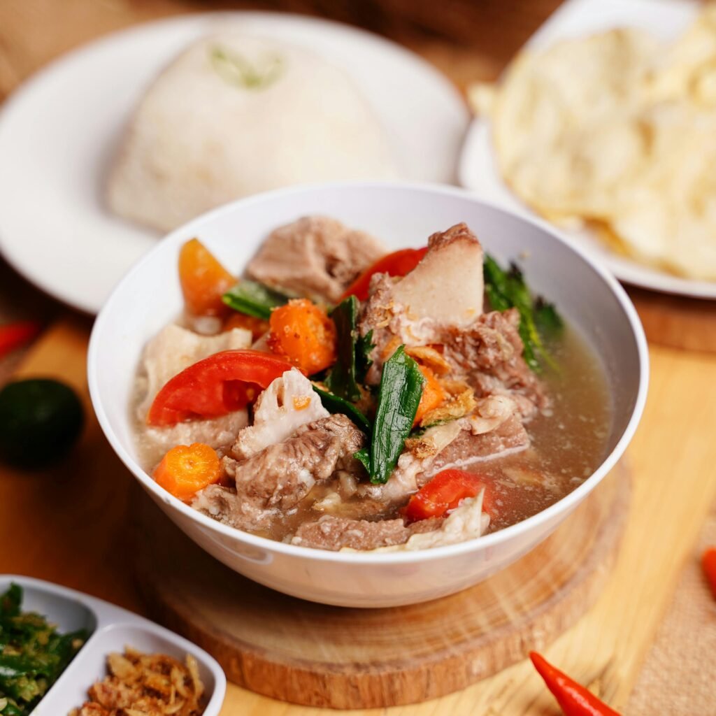 Delicious Indonesian Sop Buntut served with rice and crackers on a wooden table setting.